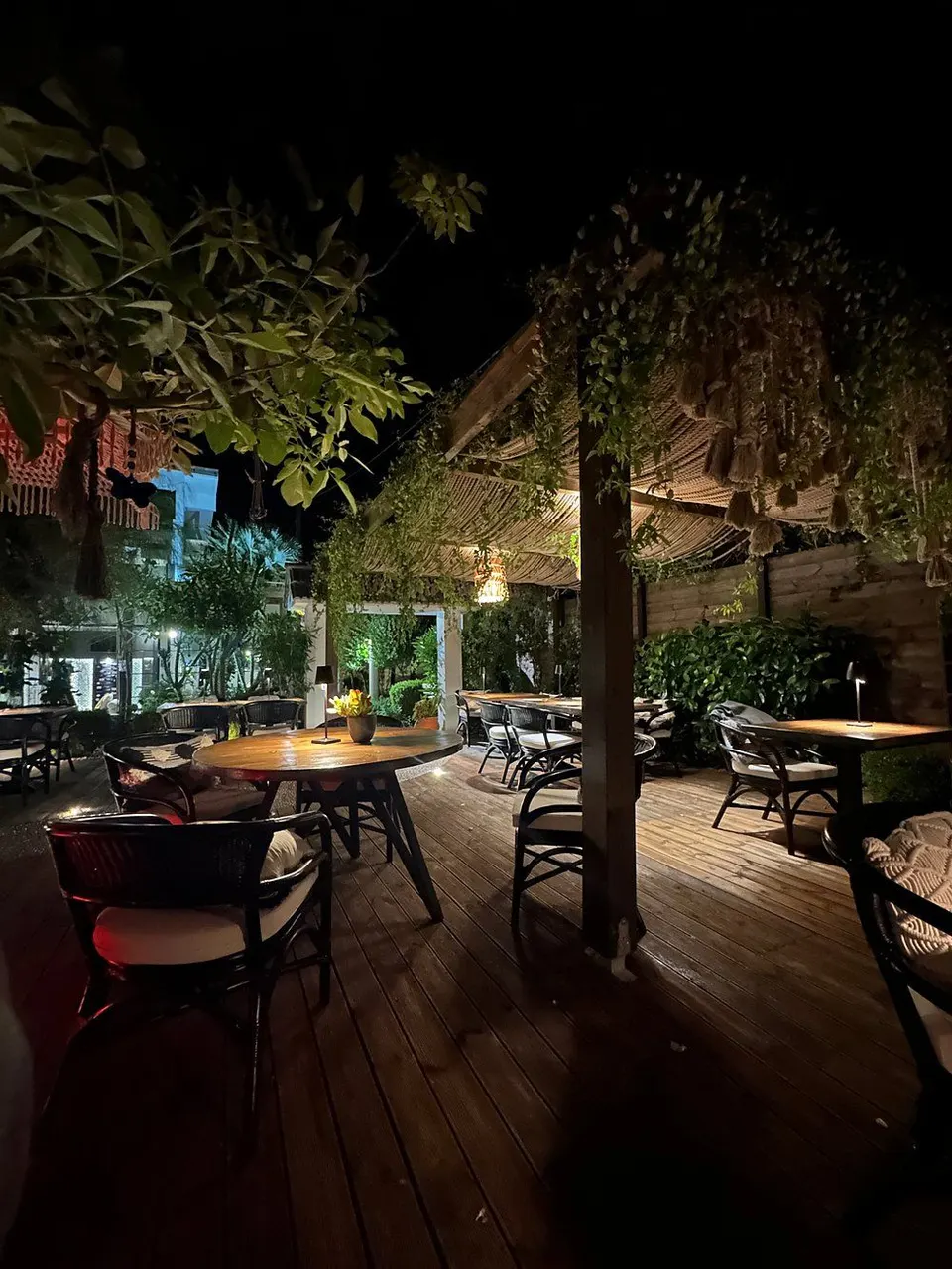 The terrace at Mariposa after dark, with wooden decking, cane shades, planting overhead and a lit table in the middle distance.