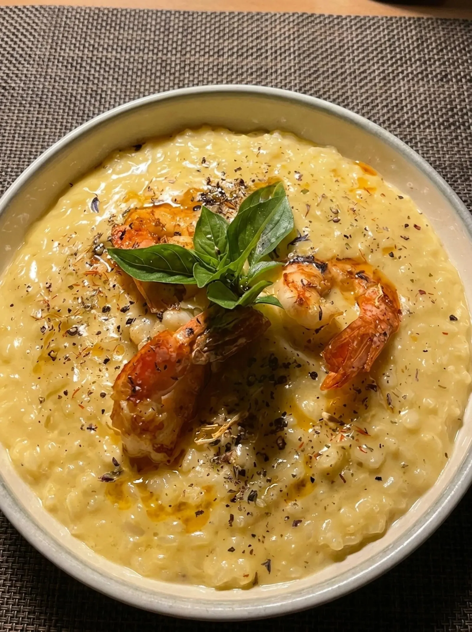 Shrimp on a saffron risotto in a dark bowl, topped with basil and cracked pepper, photographed from above.