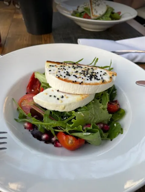 Grilled cheese over rocket, tomato and pomegranate on a wide white plate, photographed at the table.