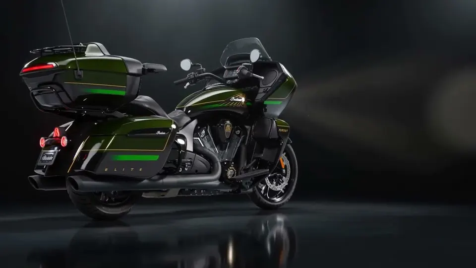The green and black Indian Elite on a dark reflective studio floor, three-quarter rear view, gold pinstriping and the ELITE lettering on the pannier catching a single overhead light.